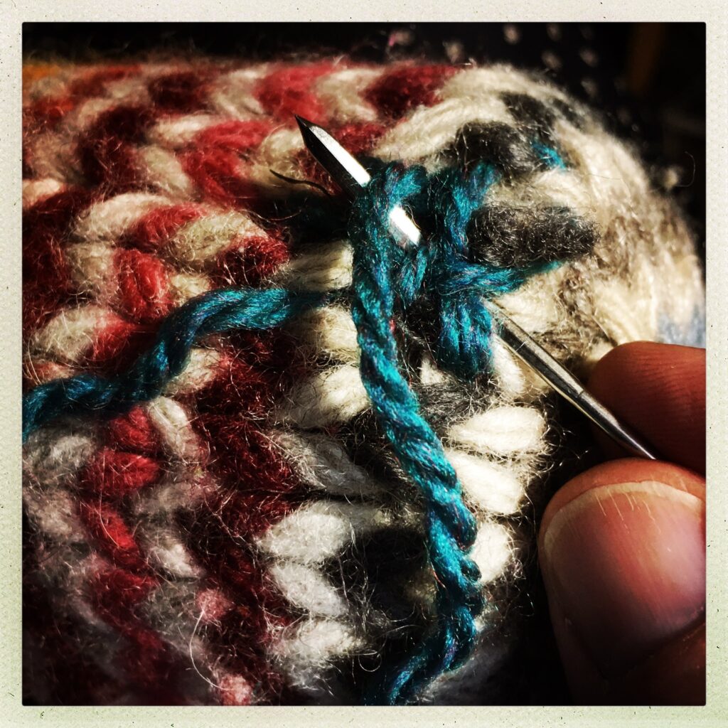 Close-up of a hand darning a wool sock with blue thread and a needle